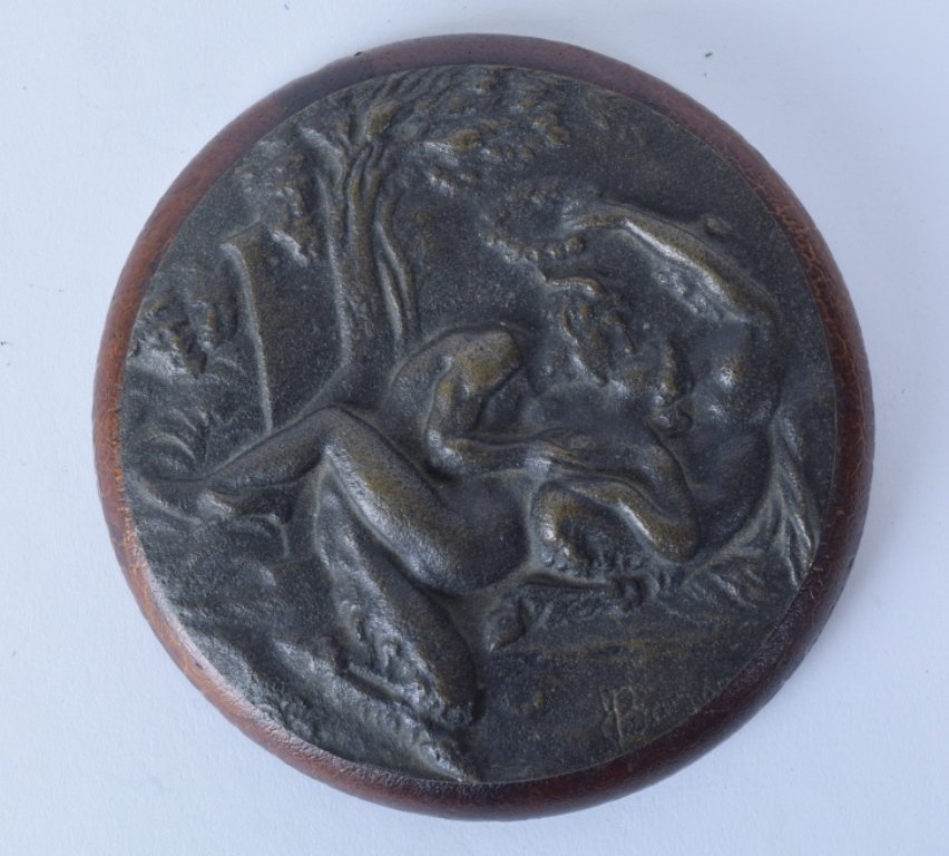 19th C. Bronze Plaque of Dionysian Scene: Erotic bronze plaque depicting a satyr and two nude women in a forest, two other faces formed into the plaque on the left. Signed illegibly lower right. Round bronze plaque on a wood mount. Dark brown
