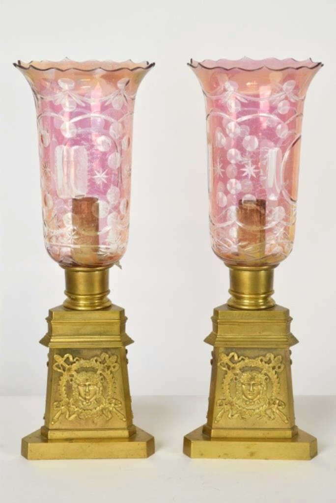 Pair Gilt Empire Lamps with Cranberry Glass Hurric: Pair of triangular gilt bronze lamps having mounted reticulated portrait medallions and cut cranberry glass shades with scalloped rims. Etched mark on the base of each lamp a crown over a "G" Electrif