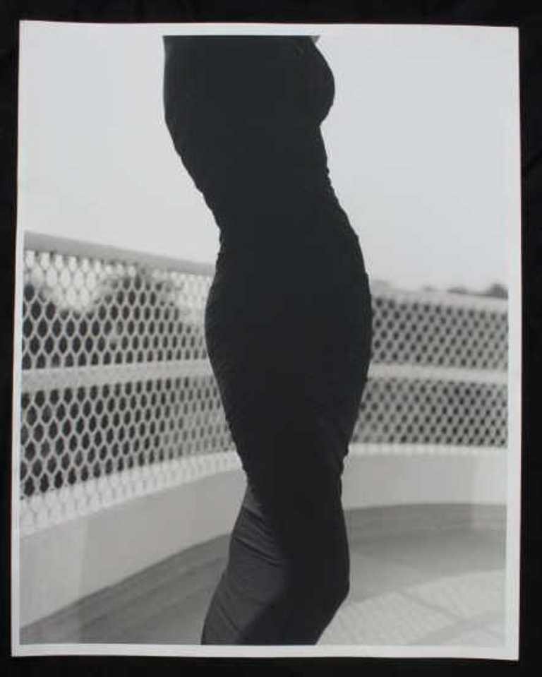 Michel Comte (1954-) Baryta Print: Black and white photographic print on baryta paper by Michel Comte. Depicting a woman's figure in a black dress from the chest to knees in front of a white chain fence. Artist's marks in pencil to ver