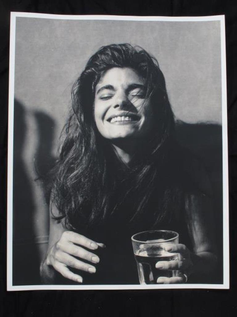 Laura San Giacomo by Michel Comte: Black and white photographic print on baryta paper by Michel Comte. Depicting a portrait of actress Laura San Giacomo laughing and holding a glass of water. Artist's marks in pencil to verso. 20 inche