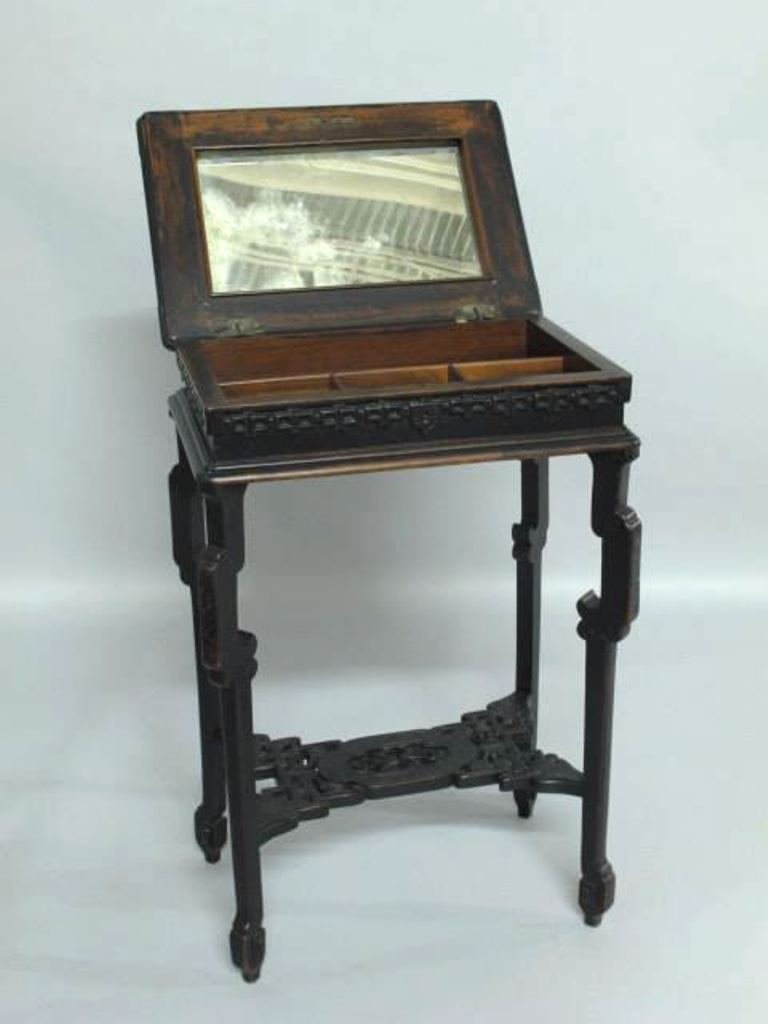 Chinese Style Vanity Stand: Chinese style black wood stand having hinged lid opening to sectioned interior compartment with mirror to underside of lid. Geometric carving to top and legs and detailed foliate carving to stretcher 