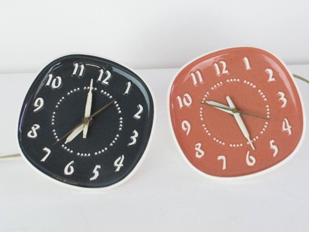 Two Vintage Russel Wright Ceramic Wall Clocks: One with a black face, one with a peach color face. Both with general electric works. Each measures 8 inches height, 3.5" inches width. Not working. 8"H x 3.5"W Good - some wear to the hings Dimension