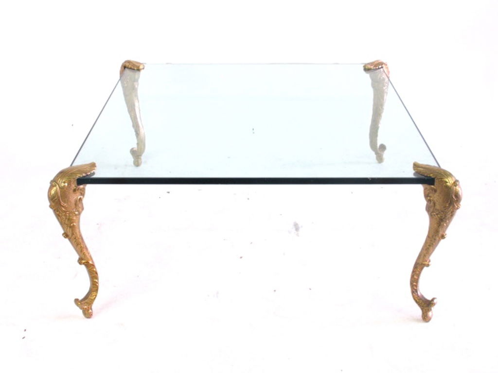 Jansen Style Brass and Glass Coffee Table: Square glass top with a fixed scrolling brass legs having relief foliate decoration. Good condition with one corner of glass chipped; unnoticeable unless legs detached. Does not interfere with structu