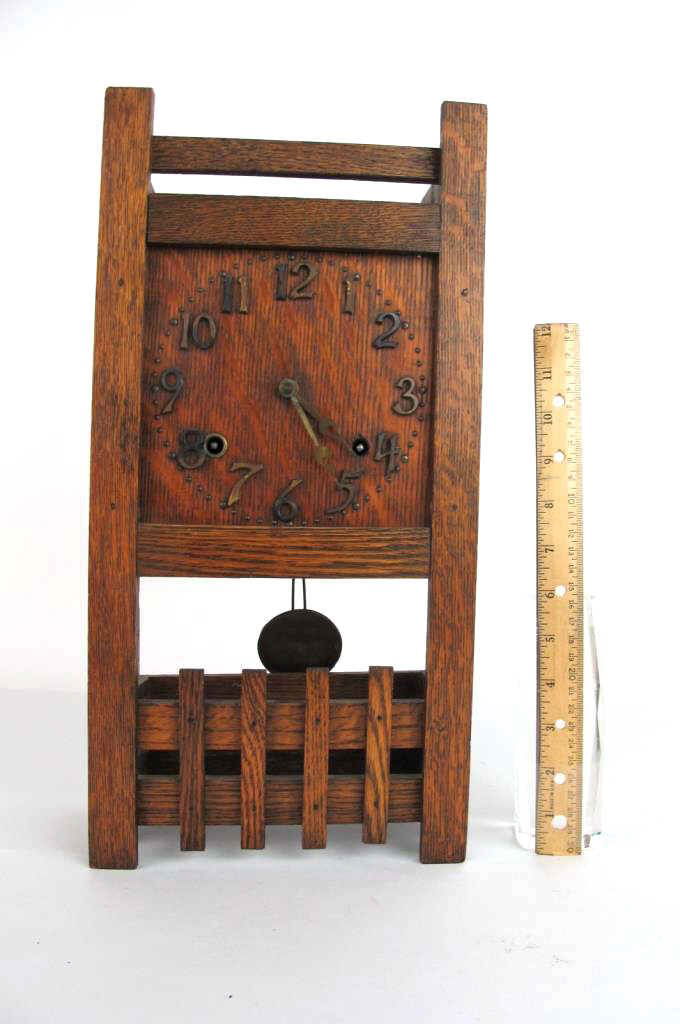Miniature Longcase Style Clock: Small oak wall clock in form of longcase clock with brass numerals and hands to face and barred detail to lower front, back, and sides. Visible pendulum. Rectangular in form. 17 inches height, 8.5 inc