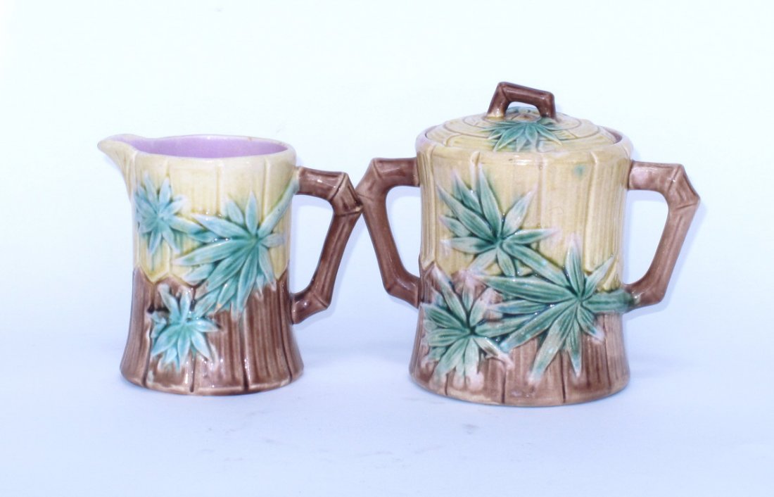 Two Pieces of Etruscan Majolica: 19th century. Both faux bamboo motif and stylized bamboo handle. All in brown and yellow tones. Makers mark to base. Lidded sugar pot and creamer. Small chips. 6 inches height. 6"H Commensurate with a