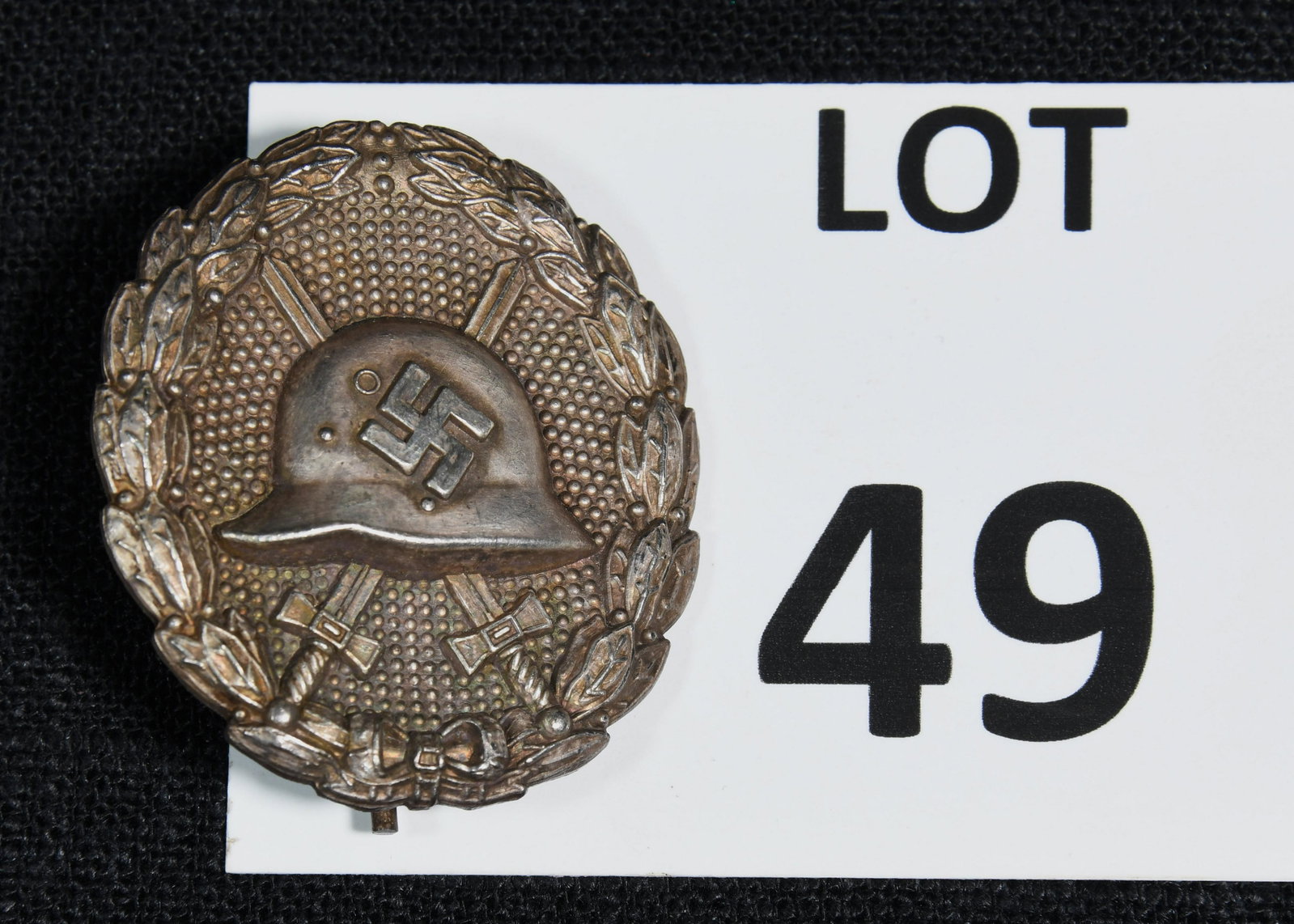 WWII German Deschler/Wiedmann Wound Badge: WWII German Deschler/Wiedmann wound badge. This badge is made of zinc and features a helmet with a swastika at the center placed in front of two crossed swords. The badge is bordered with an oak leaf 