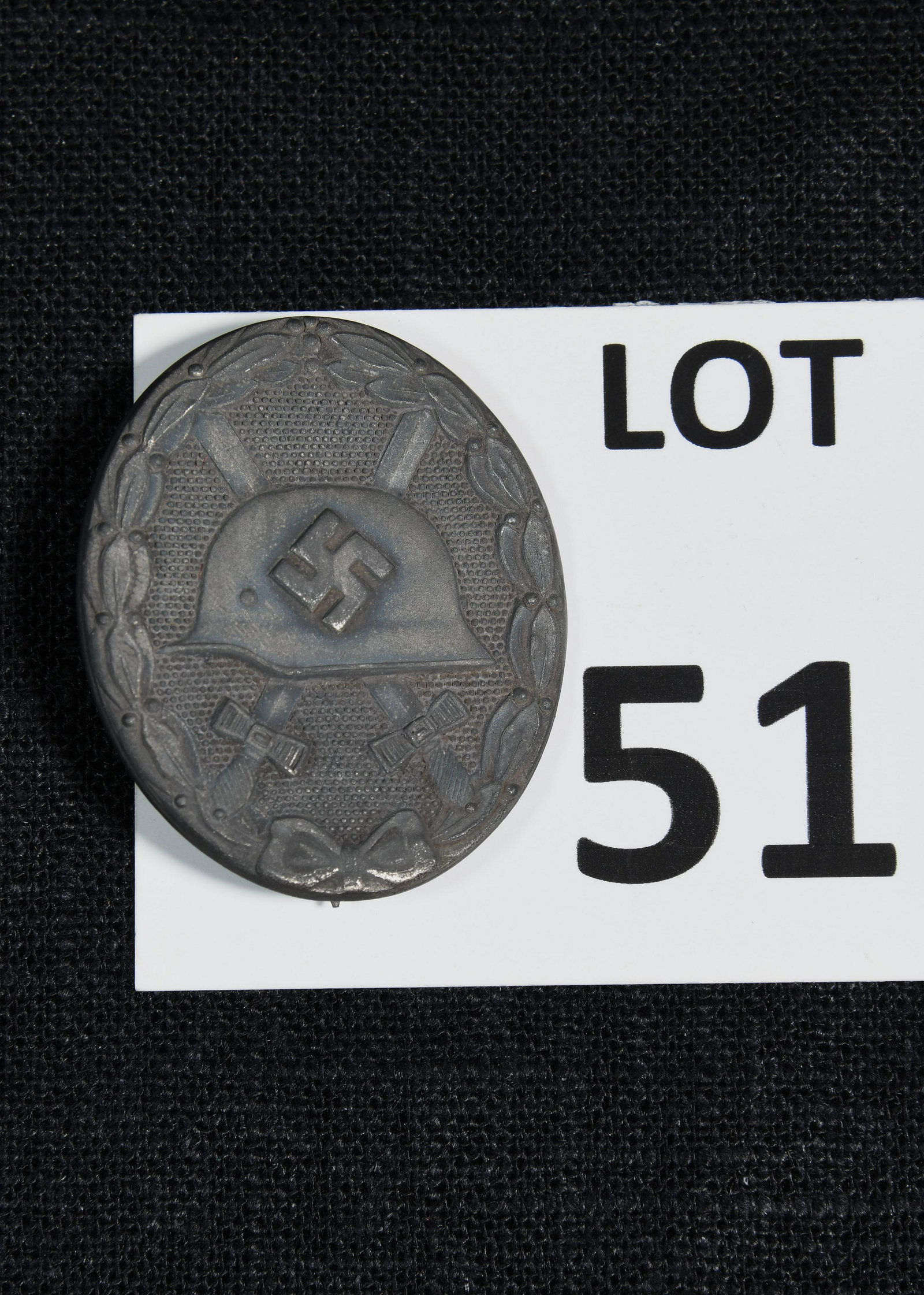 WWII German Wound Badge 3rd Class: Black WWII German wound badge, 3rd class. This badge features a helmet with a swastika at the center that sits in front of two crossed swords. The reverse side of the badge is stamped with "65". *note