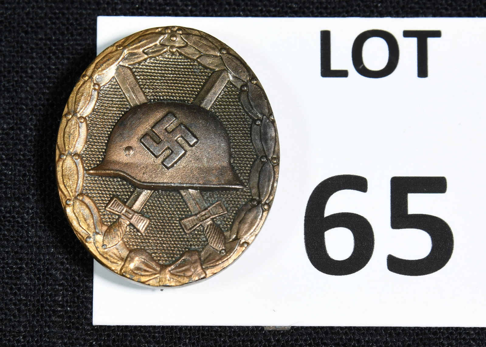 WWII German Wound Badge: A WWII German wound badge. This badge features a helmet with a swastika on it and sits in front of two crossed swords. It has an oval oak leaf wreath border. The reverse is stamped "30". *notes- tarni