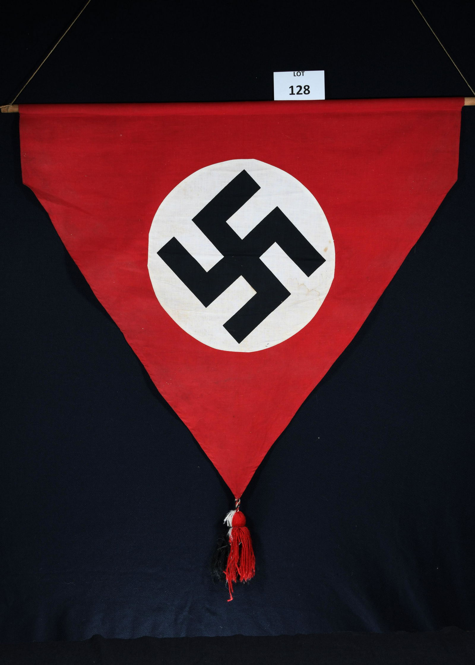 Antique WWII Era German Nazi Podium Flag: An original antique WWII era German Nazi podium flag. Flag is triangle shaped and has tassel at the bottom point. Hung on a wooden pole.Flag measures 38"x31". *notes- some staining and wear throughout