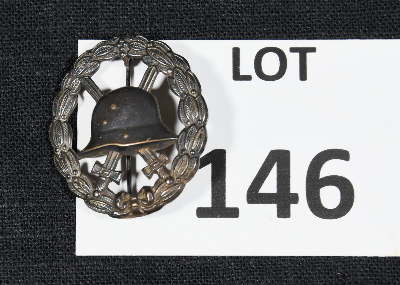 WWI German Wound Badge: A WWI German 3rd class wound badge in black. This badge has an oak leaf wreath with a helmet at the center in front of and two crossed swords. Reverse side of badge is unmarked. *notes- finish loss to