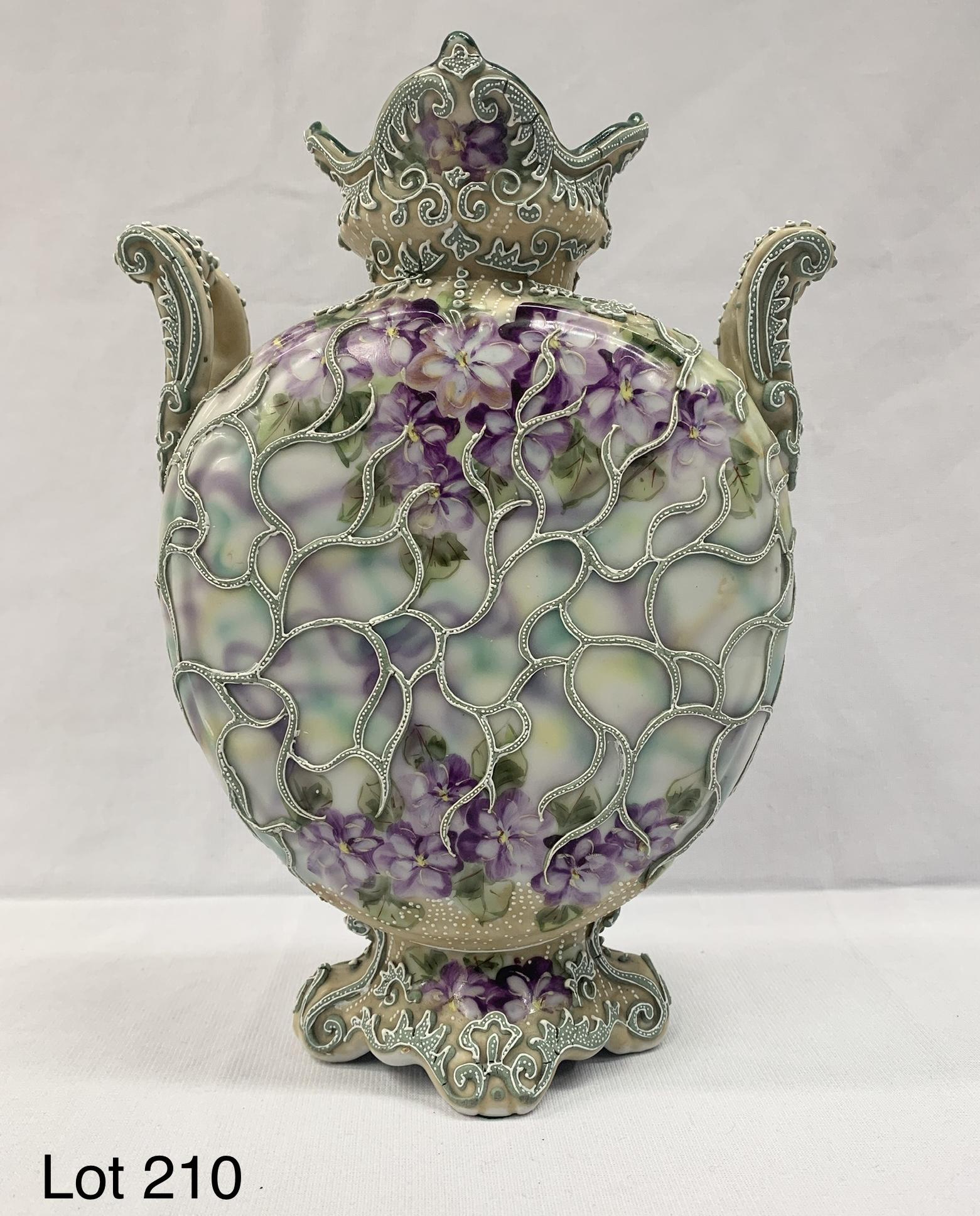 Antique Nippon Moriage Porcelain Vase: An antique Japanese Nippon moriage porcelain vase. This vase features hand painted purple floral decoration throughout its circular body. It has scrolled arms on each side and a footed base. Beautiful
