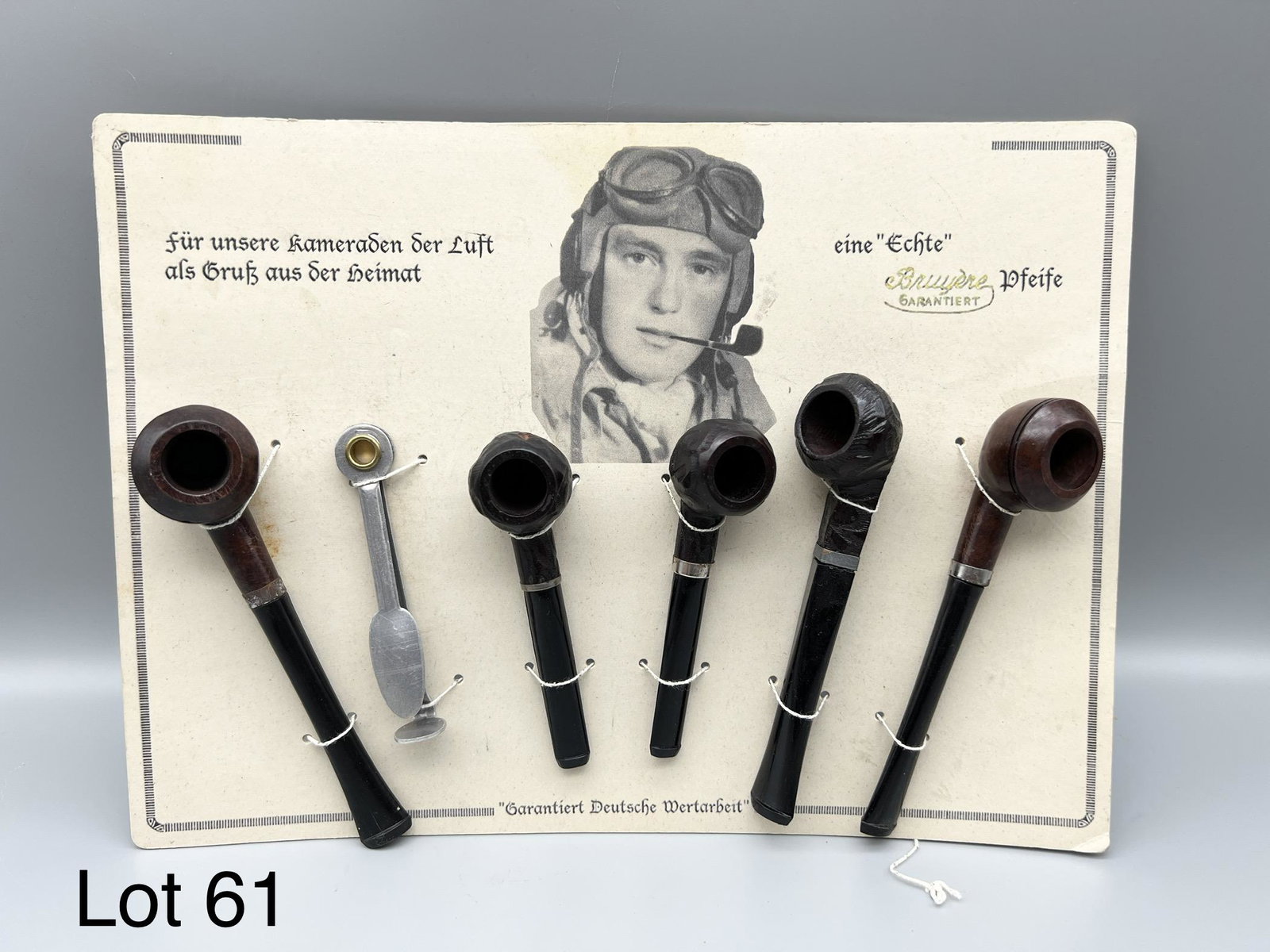 WWII German Bruyere Smoking Pipe Set: WWII German six piece set of Bruyere smoking pipes. The pipes are in the original packaging with cardboard backing featuring a pilot smoking a pipe. The bottom reads "Guaranteed German Workmanship" in