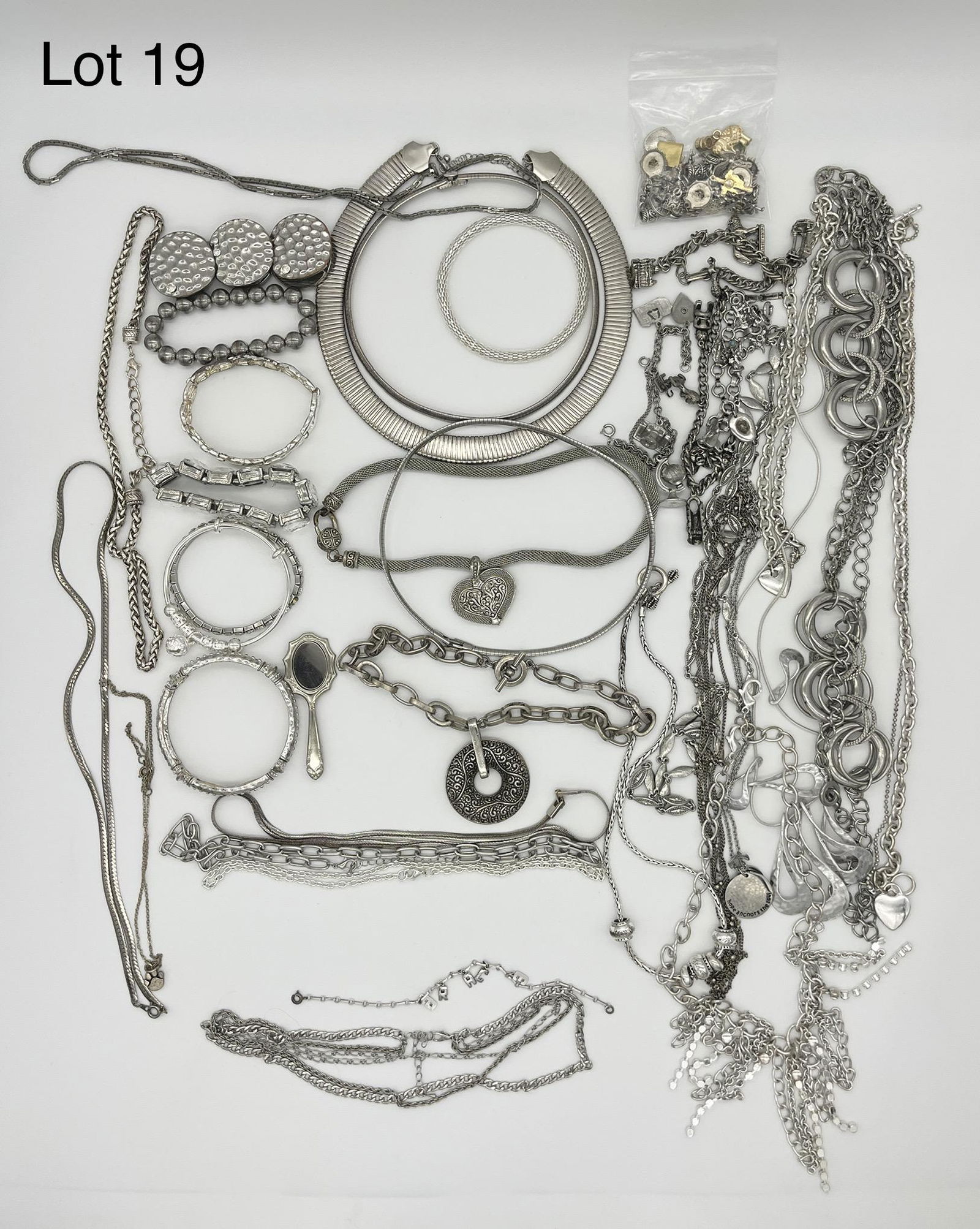 Lot of Silver Toned Costume Jewelry: A lot of shining silver costume jewelry with crystal elements. Lot includes long chain necklaces, bracelets, and more. Lot also includes several silver charm bracelets with a bag of charms.