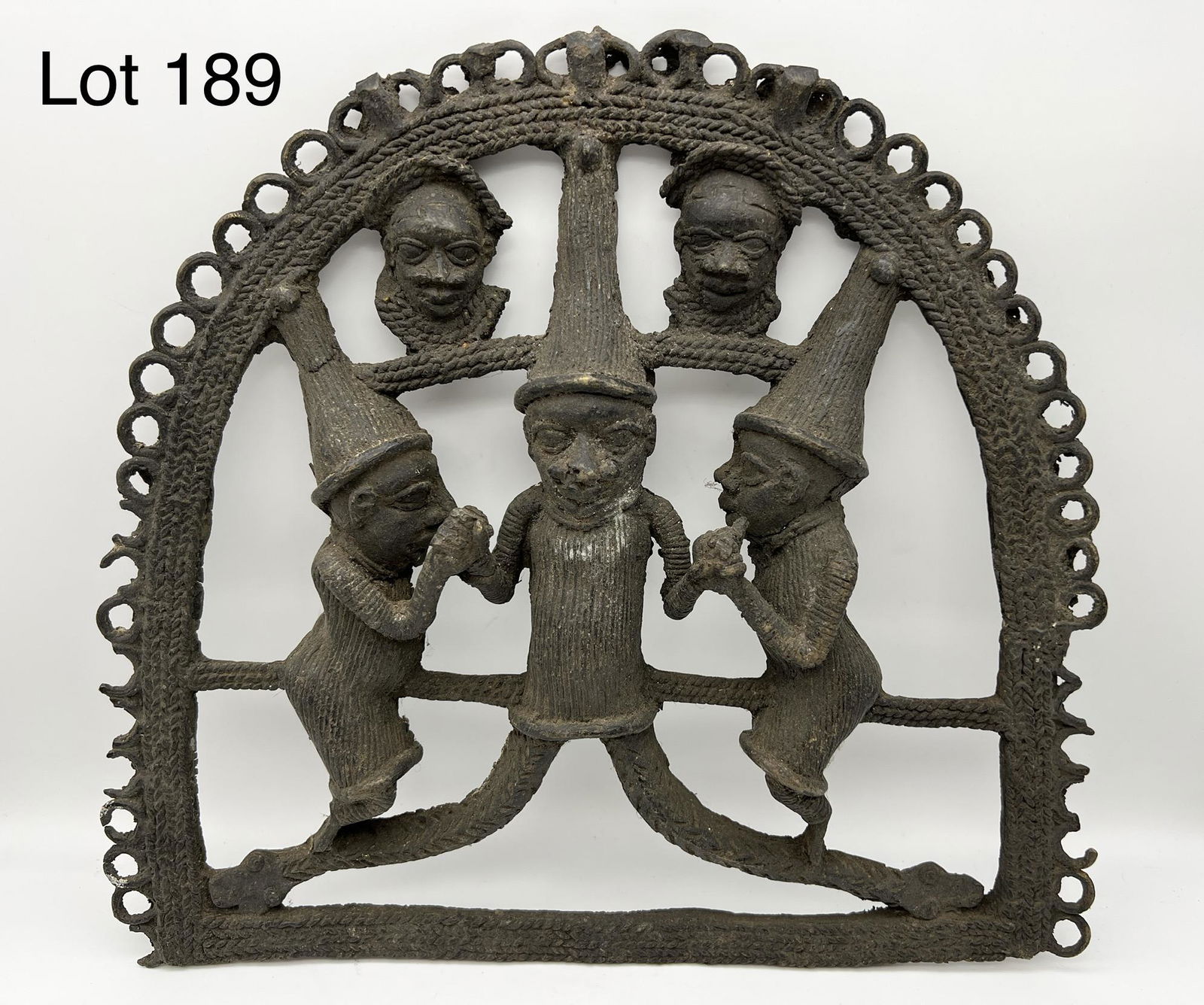 African Bronze Plaque: African bronze plaque featuring a man with snake legs holding the hands with men on each side. The top has two heads. Arch has decorative rings along outer edge. Measurements are 14" x 14 1/2" x 1 1/2
