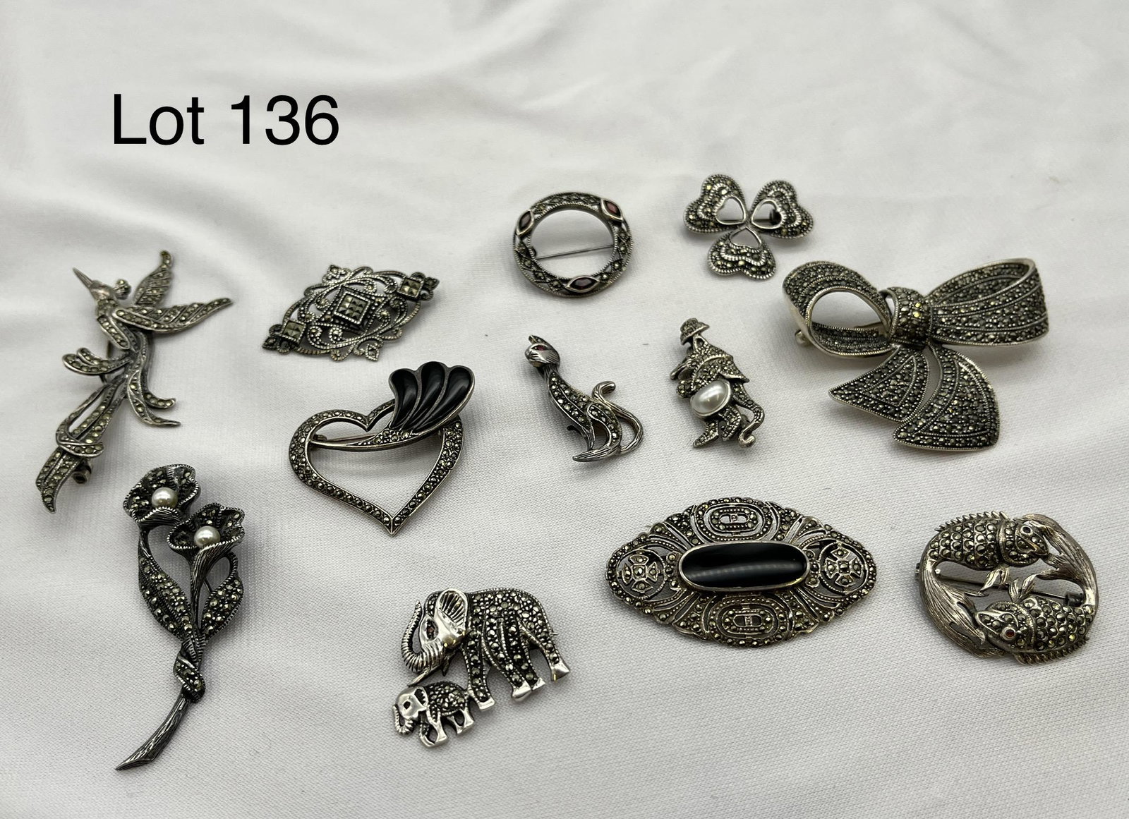 Collection of Vintage Sterling Silver Pins: A collection of vintage pins made from sterling silver showing a wide range of shapes, including a mouse, a pair of elephants, a black onyx pin, and much more. Two pins, the hummingbird and the flower