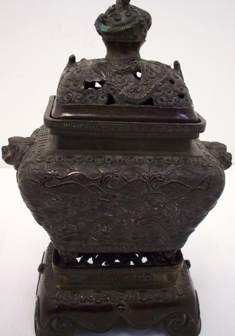 18th Century Bronze Incense Burner with Stand: China, 8" tall X 8" wide X 5" deep with a 2 1/2" tall X 5 1/2" X 4" stand, heavily decorated with splashing waves, animals, birds, lizards, patterned designs in relief, side Foo Dog Handles, base and 