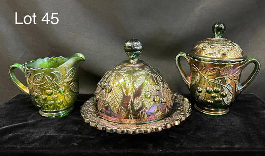 Trio of Carnival Glass With Cherry Chain Pattern: Lot of three Carnival glass items. Includes 1) an emerald butter dish with domed lid. 2) an emerald sugar bowl with lid. 3) an emerald creamer bowl with handle. Tallest is 7". *notes- no chips or crac