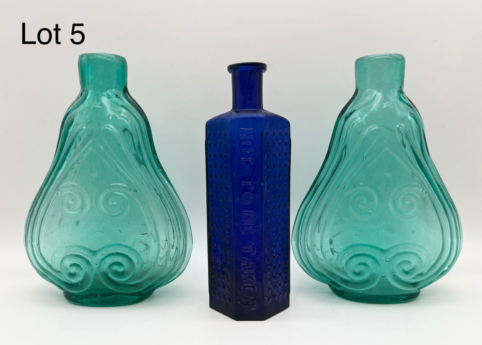 Mixed Lot of Glass Bottles: A mixed lot of three glass bottles, including: a pair of reproduction aqua glass scroll flasks and a cobalt blue glass poison bottle marked "NOT TO BE TAKEN" with a textured star pattern, number 6 at