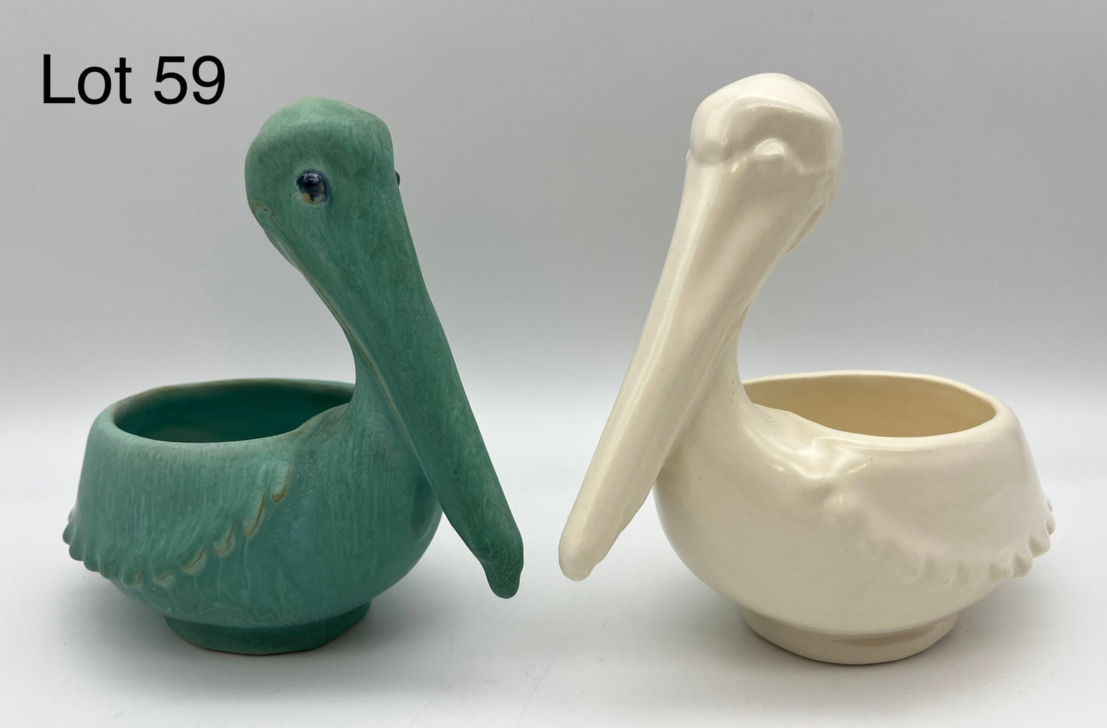 Pair of Weller Patricia Pelican Planters: A pair of Weller "Patricia" planters made after perched pelicans. One in evergreen glaze with prismatic glass eyes, while the other is entirely in eggshell. Signed makers marks noted underneath each, 