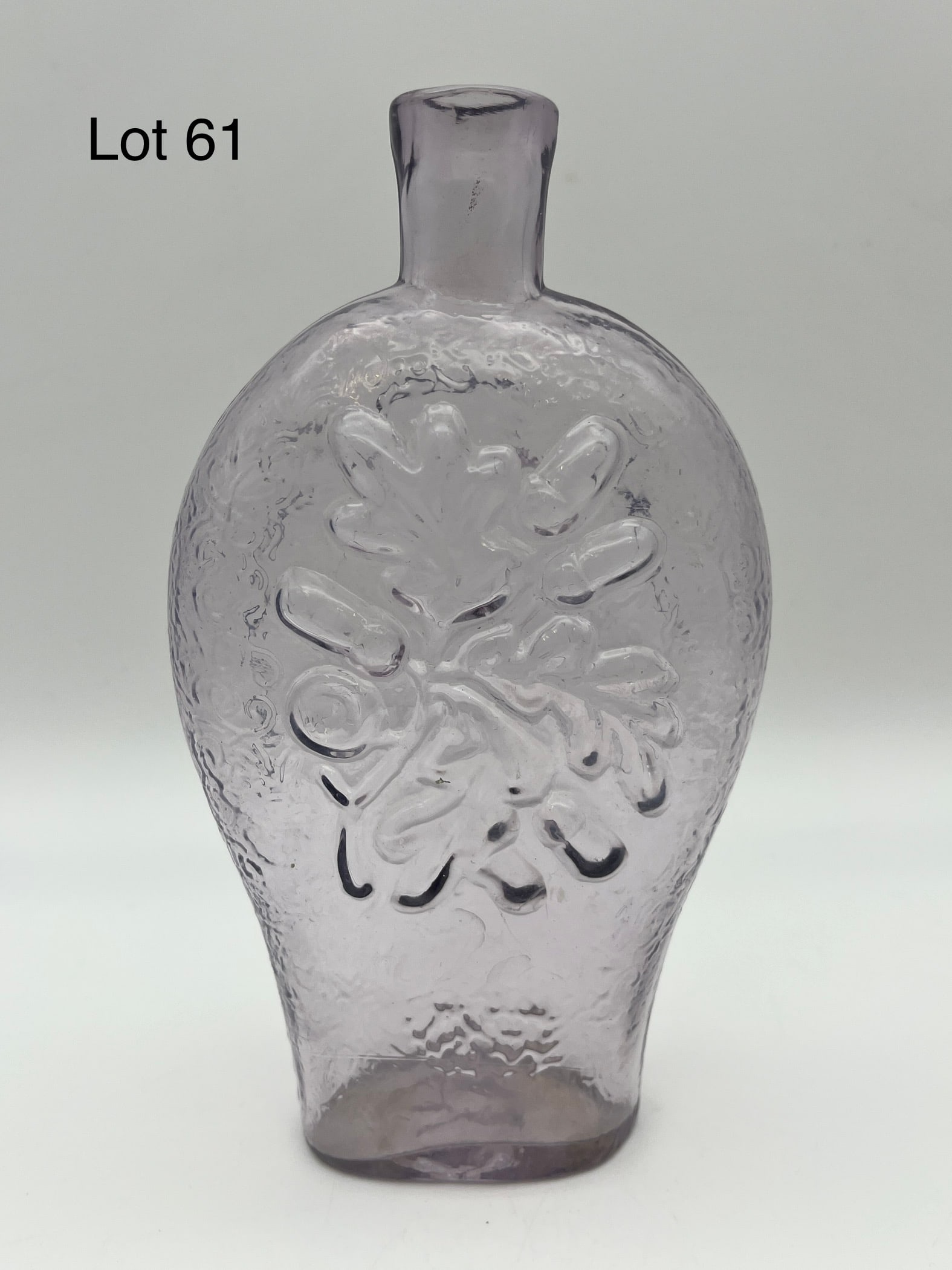 Antique Clear Glass Acorn Flask: An antique open mouthed clear glass flask, one side with an oak branch and acorns and the other showing a crest. No makers marks noted, measures 7" tall. *note - no chips/cracks