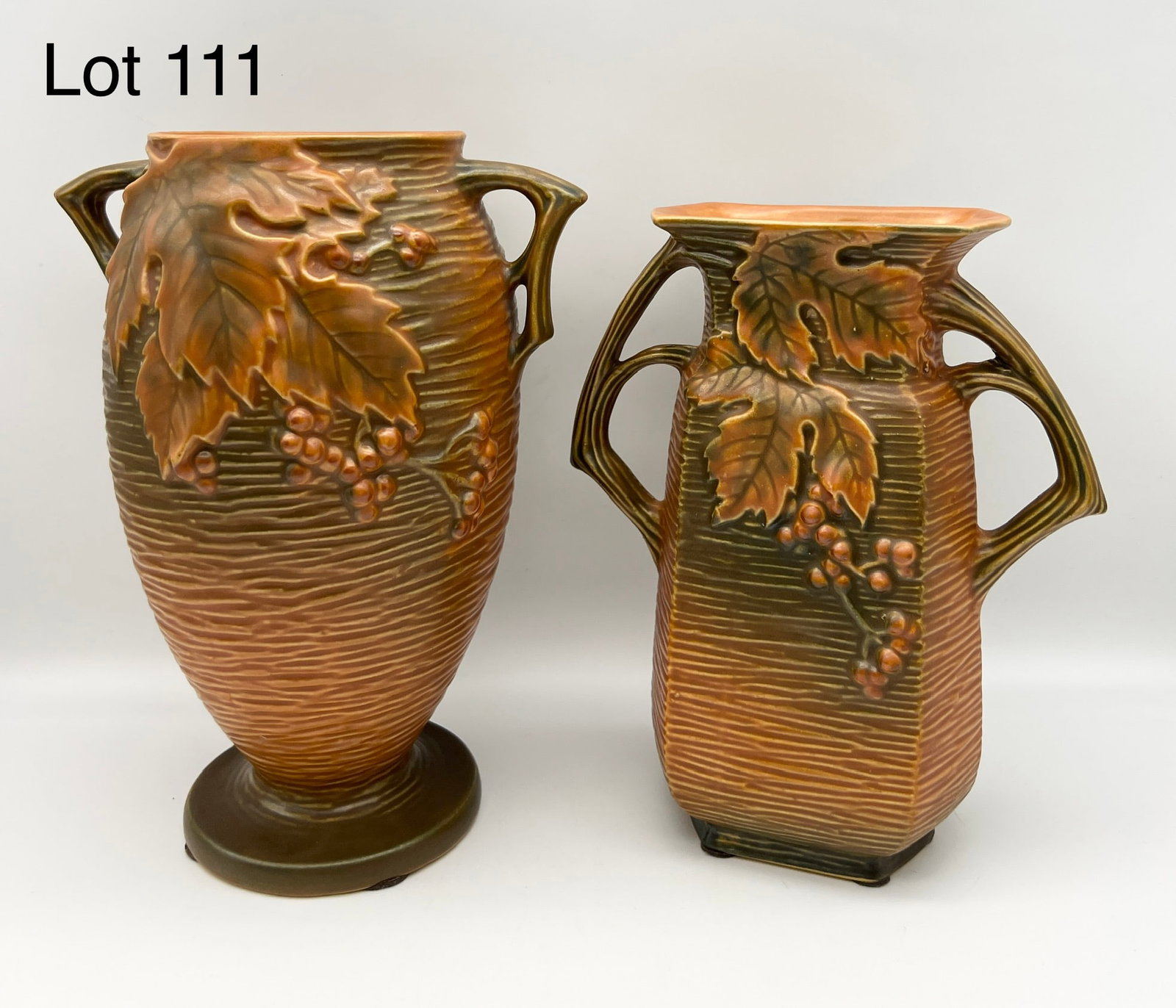 Duo of 1940s Roseville Bushberry Russet Vases: Lot of 2 Roseville pottery bushberry russet vases (35-9 and 33-8). Both vases feature leaf and berry design, dual handles, textured finish and russet glaze. 9 1/2" and 8 1/4" tall. Makers mark on unde