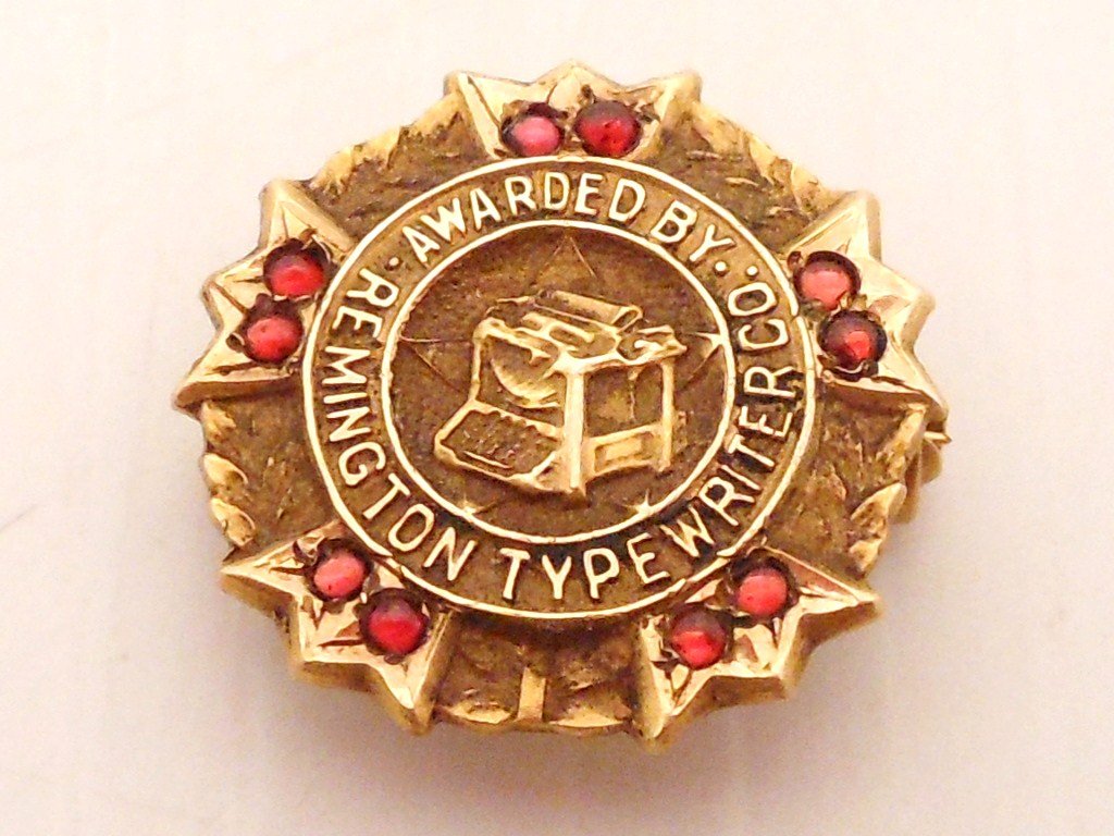 14Kt Yellow Gold Remington Typewriter Pin: 9/16" across, pin reads Awarded By Remington Typewriter, yellow gold pin with 10 small red stones, marked, 1.35 dwt.