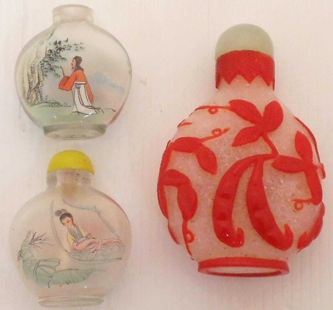 Lot of Glass Snuff Bottles: Lot Of three. Two 2" reverse painting snuff bottles. Each has a different landscape scene on each side. One is missing its cap. 3" White snuff bottle decorated with plants, pods and a grasshopper all 