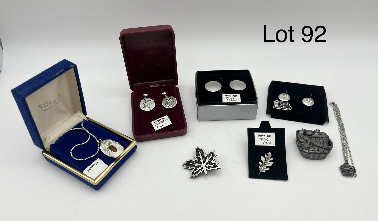 Assortment of Pewter Jewelry Featuring Earrings: An assortment of pewter jewelry that includes necklaces, pins, and several pairs of earrings. Notable pieces include a Blackington pinecone necklace, a pair of Nobska engraved ship earrings, and an ap