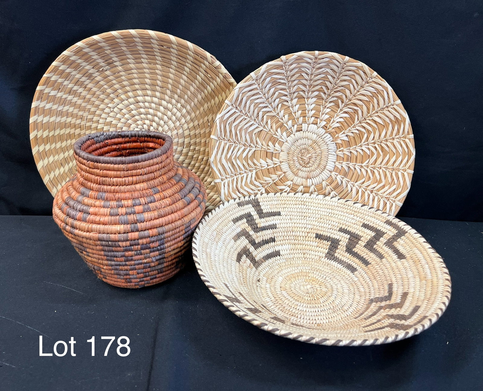 Collection of African Native Coiled Baskets: Group of four African native coiled baskets. Includes three round tray bowl shaped gathering baskets and a coiled pot shaped basket. Larges tray is 17 1/2" diameter, pot basket is 7" tall.