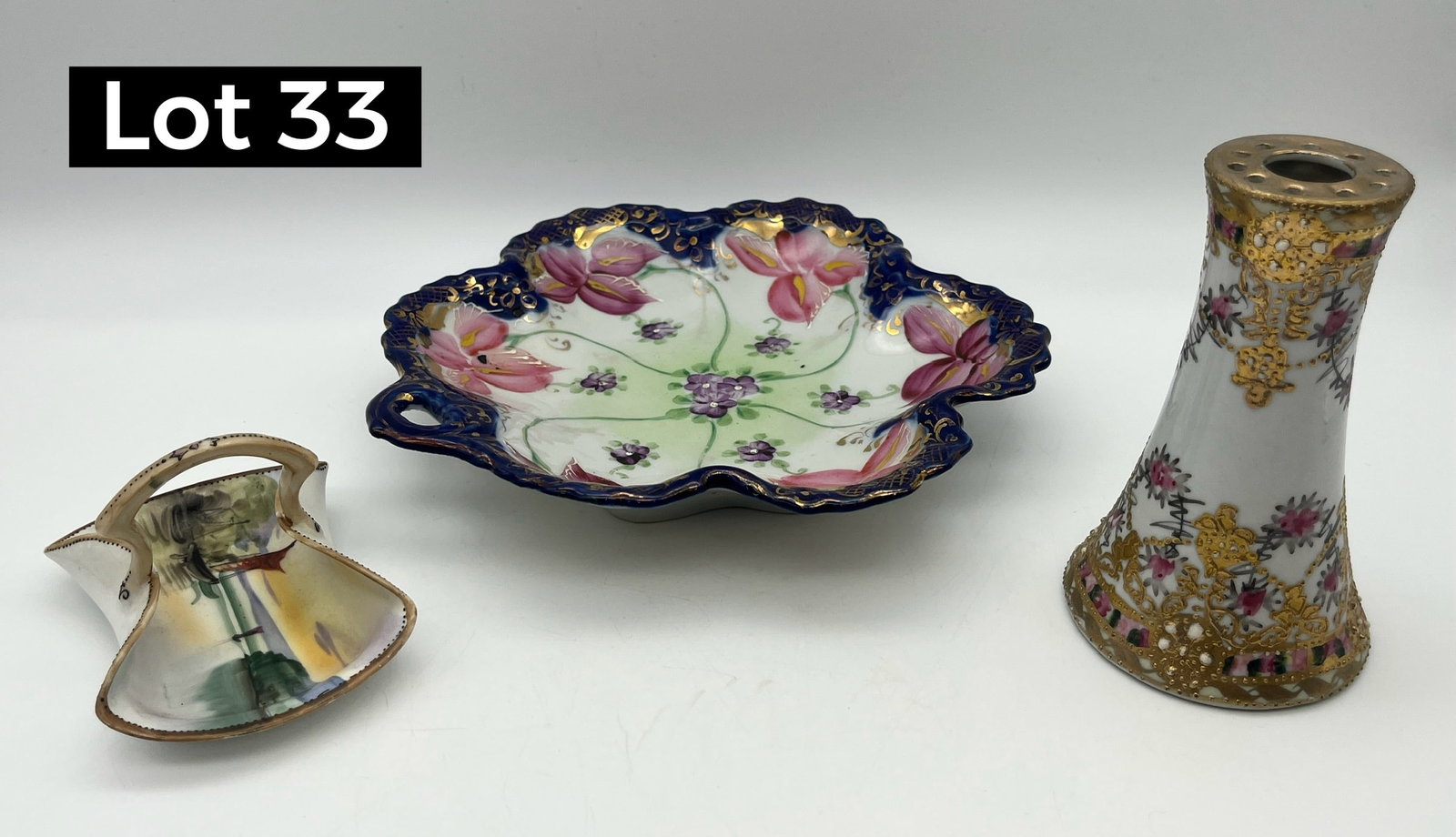 Trio of Decorative Nippon Porcelain Wares: Three elegant Nippon porcelain pieces, including: a cobalt blue and gold trim bowl, a floral pin holder, and a miniature trinket basket with a coastal scene. Bowl measures 8 1/4" across, pin holder 5"
