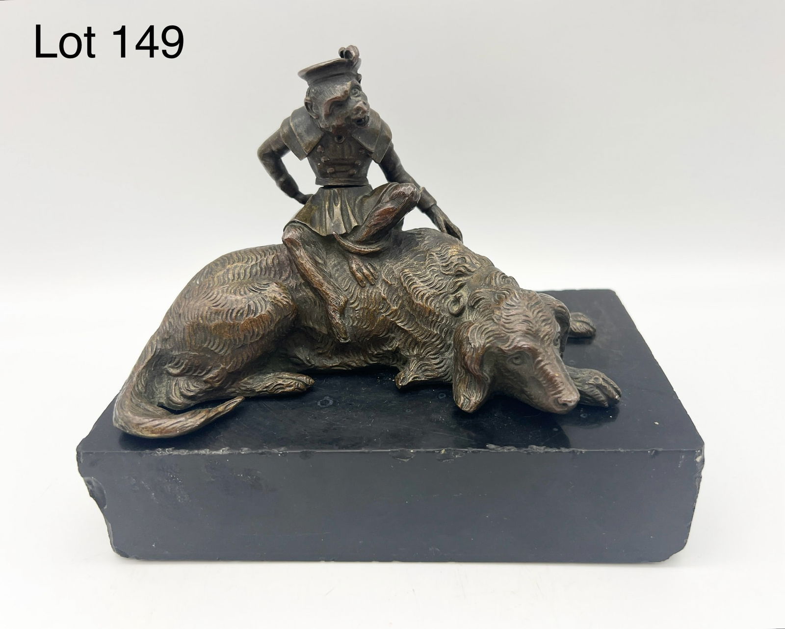 Bronze Statue of Monkey and Dog: A bronze statue of a clothed monkey sitting on a reclining dog. Monkey swivels at waist. Piece attached to a rectangular black marble base. 5" x 6 1/2" x 3 3/4". *notes- some wear and chipping on base
