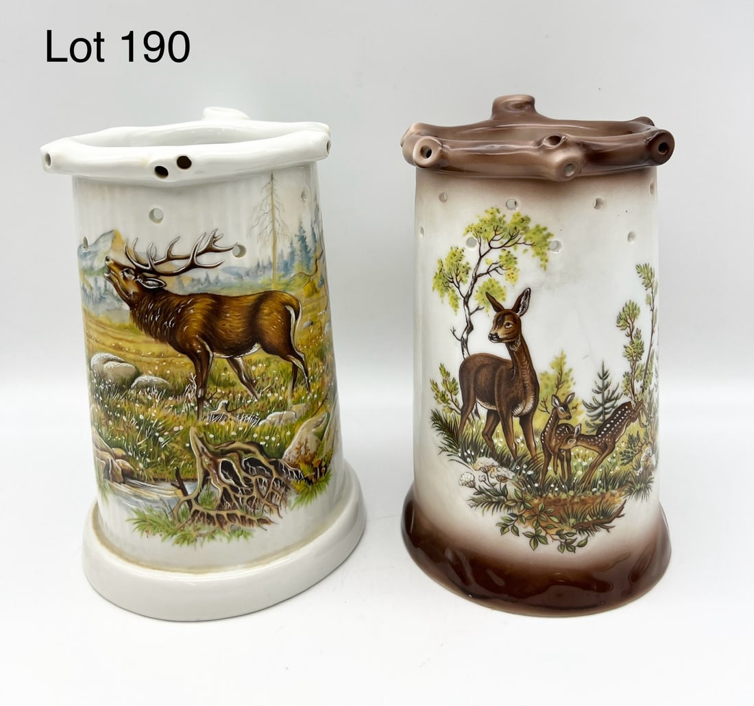 Pair of Germany Puzzle Jugs Featuring Wildlife Motifs: Lot of two vintage puzzle jugs with wildlife scenes of a doe with two fawn in the woods and an elk buck by the water's edge with mountain view in the background. The deer jugs is marked "Made in Bavar