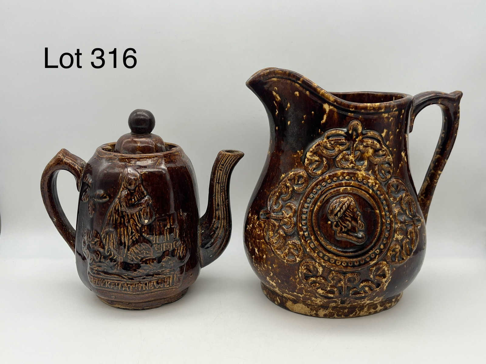 Pair of Rockingham Ware Splatterware Ceramics: Two pieces of unique Rockingham ware splatterware ceramics in distinctive brown glaze and relief design work. Includes a teapot with an image of a woman and text that reads "Rebekah at the Well", and 