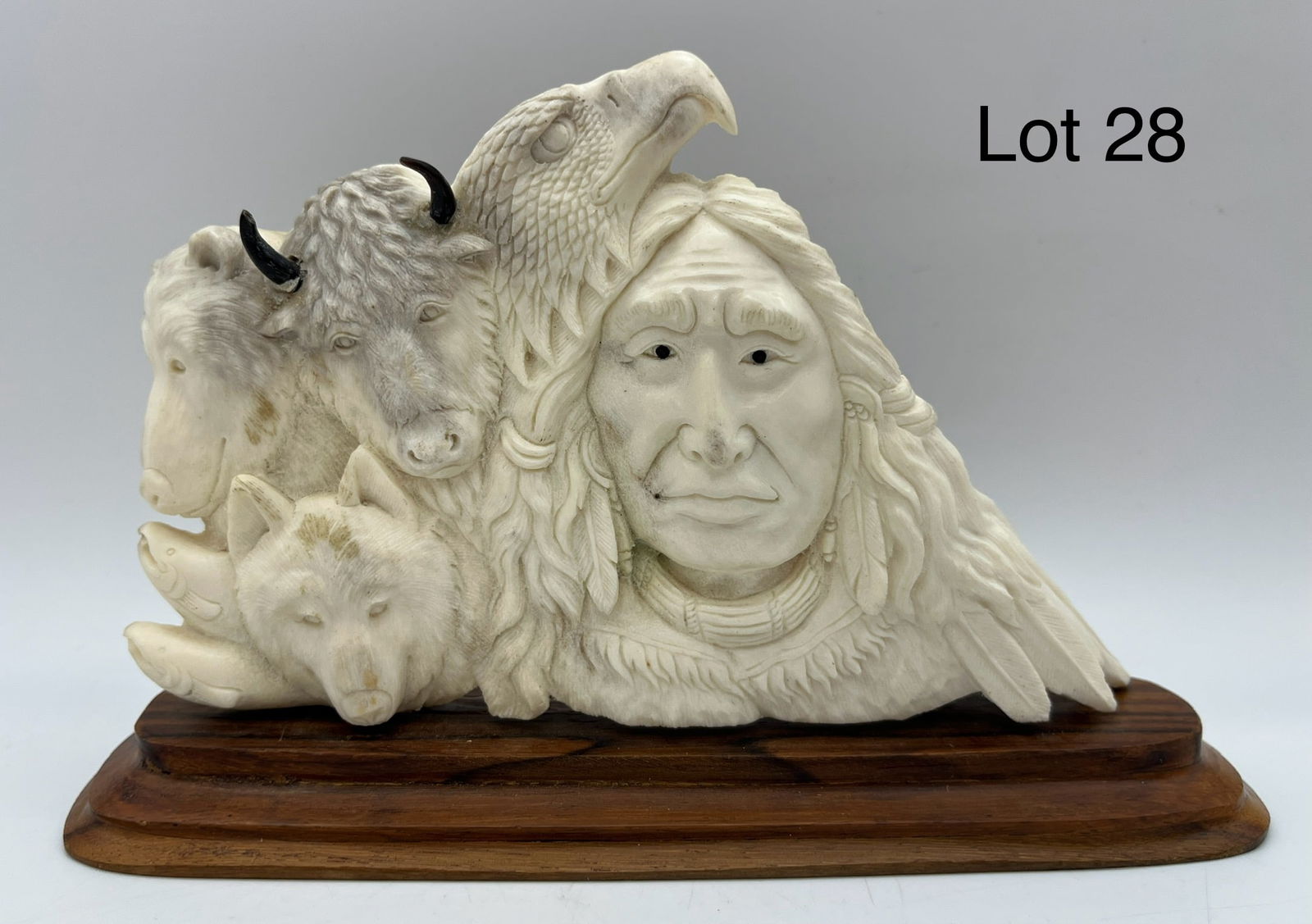 American Indian Moose Antler Carving: An American Indian polished carving of a moose antler. Sculpture shows relief of a wolf, a bear, trout, a wolf, and a man. Mounted on wood base, measures 7 3/4" x 2" x 4 3/4"
