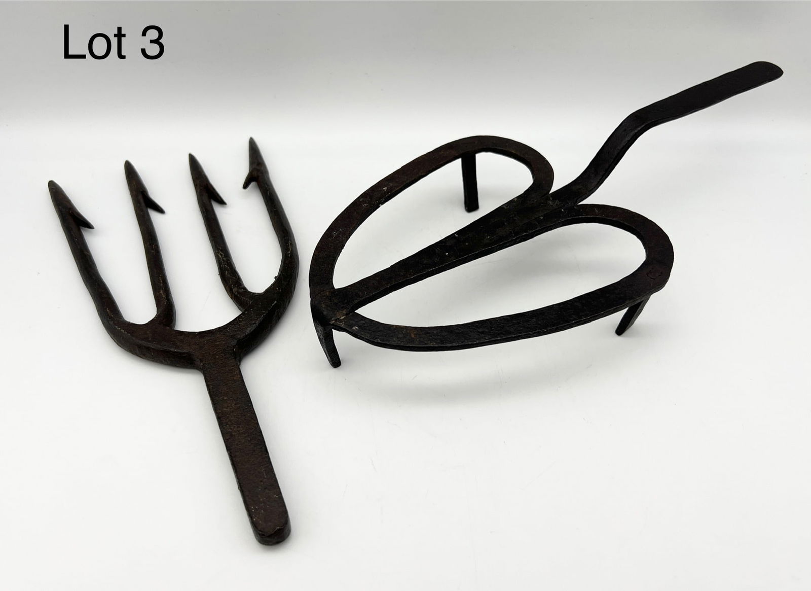 Primitive Hand Forged Wrought Iron Lot: Lot of two antique hand forged wrought iron items. Includes a heart shaped iron trivet and a four pronged fishing spear. Trivet is 10 1/2" long.