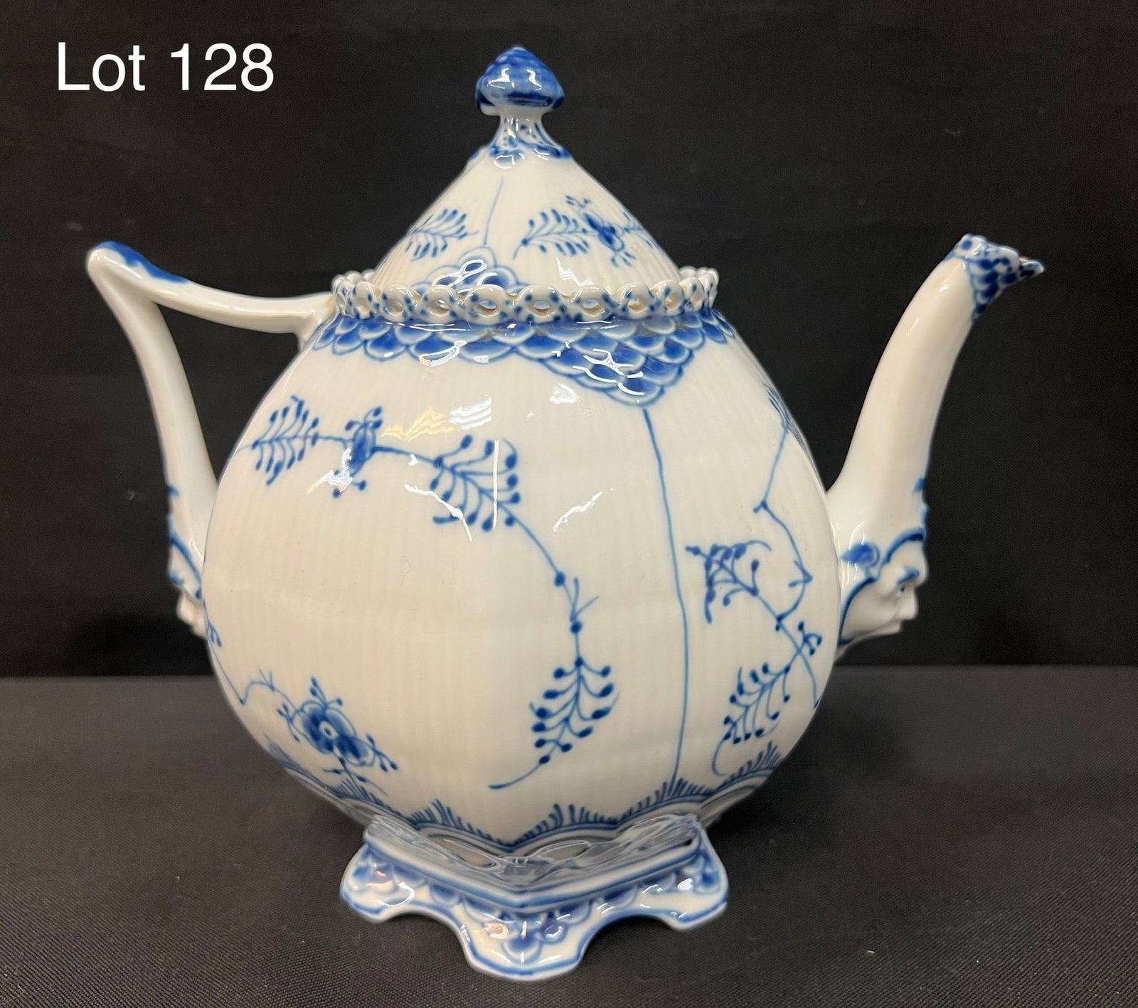 Royal Copenhagen Blue and White Porcelain Teapot: A Royal Copenhagen blue and white lace porcelain teapot. Heads at base of spout and handle. Bottom and lid bare makers marks with 1/1119. 8" tall.