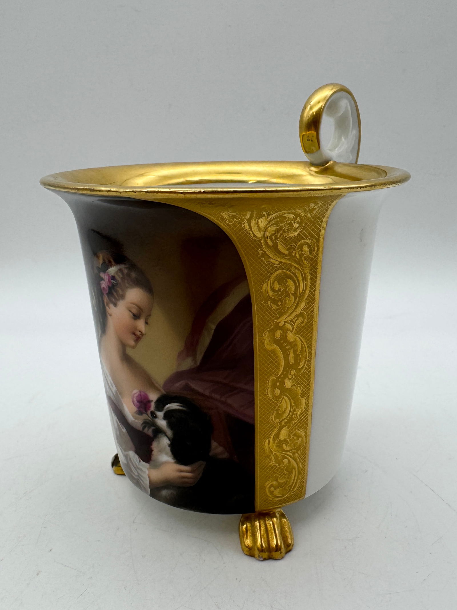 Antique German Porcelain Bildtasse: An unmarked KPM German porcelain bildtasse featuring a portrait of a young girl and her dog. Gilt accents and feet with curved handle. Measures 5" tall. *note - adhesive felt under feet