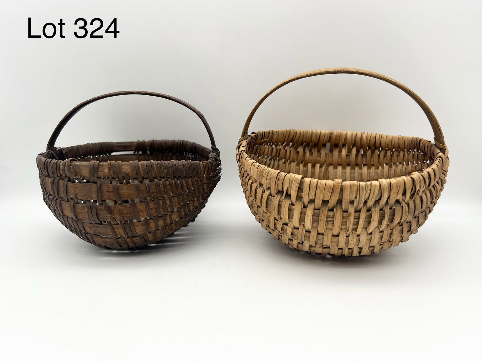 Pair of Antique Primitive Splint Weave Baskets: Lot of two small late 19th century round splint weave baskets with handles. Lighter toned basket is slightly larger and measures 6" tall including handle, 7" across. *notes- both show some loose weavi