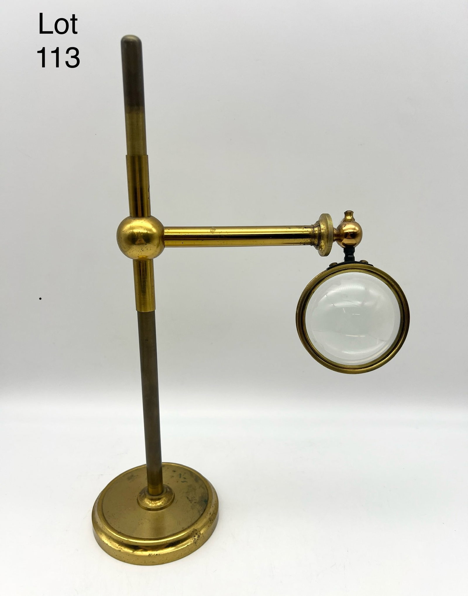 Adjustable Antique Brass Magnifying Glass On Stand: Adjustable antique brass magnifying glass on stand. Height of stand is 12" and glass 2.5" diameter. Glass arm extends. Unmarked. Brass shows some discoloration.
