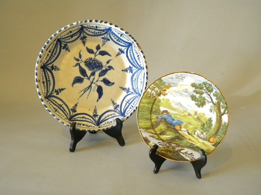 18th century European glazed earthenware plates: 1. 6 3/4" painted scene of resting traveler 2. 9 3/4" delft in blue floral sprig w/garland border