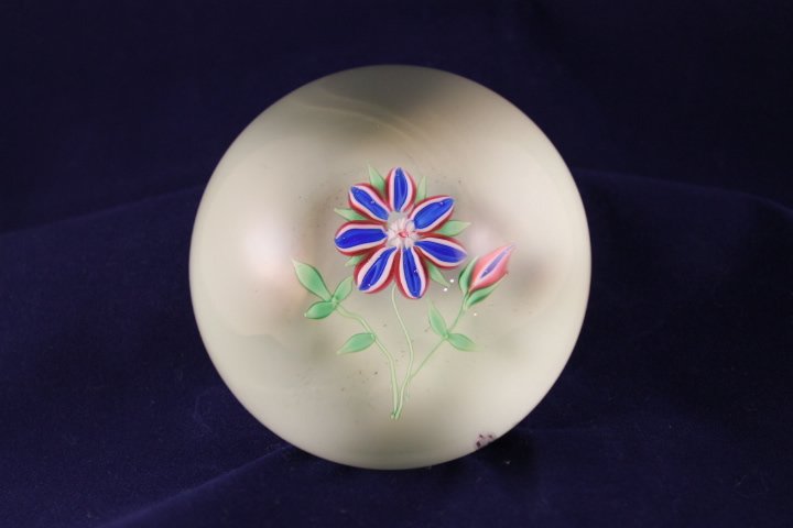 Baccarat, Modern 1971 Paperweight: Modern Baccarat 1971 paperweight. Cane 1, lampwork, flower. Red, white, and blue striped flower, 7 rounded petals, 1 bud, green leaves and stem, opaque white ground. Size is 3" wide by 2 1/4" tall