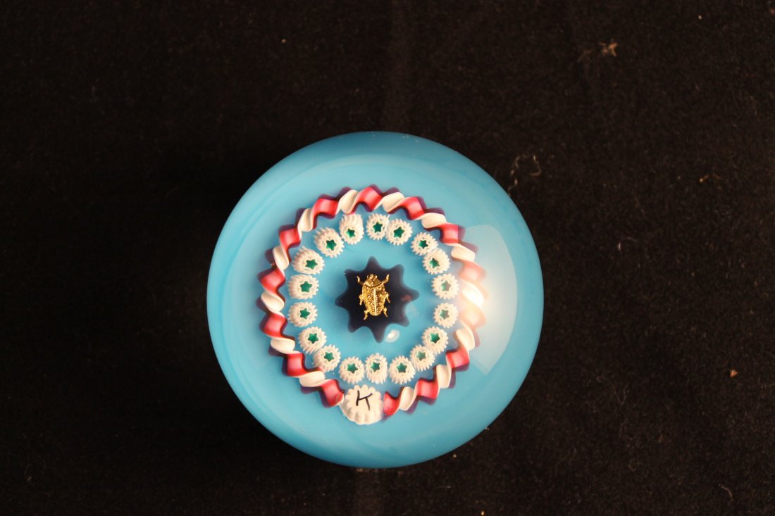 Charles Kaziun Jr Paperweight: Gold scarab with garland of white canes, pink and white torsad, blue ground Signature K size is 2 1/4"