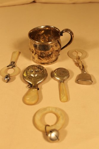 5 Rattles & one Childs Cup: 5 assorted rattles, one Tiffany & Co, Shreve, Crump & Low, all with mother of pearl handles, one a cats face, all have dents, cup has many dents