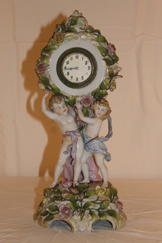 German Porcelain Clock: German porcelain clock with 2 children holding up the clock, case having many applied flowers. Size is 14" tall