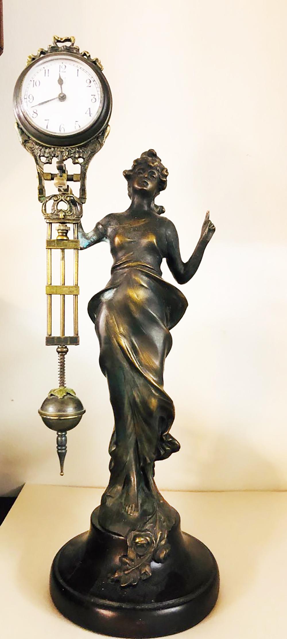Art Nouveau Swinger Clock: Art Nouveau style lady, bronze swinger clock. Lady has one hand pointing upward. Measures approx. 13 in tall.