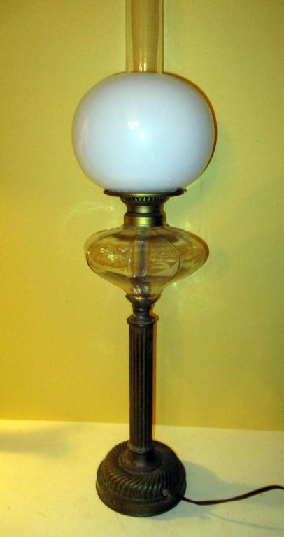 Victorian Oil Lamp: Lot consisting of brass Victorian oil lamp with a glass oil font. It has a chimney and white shade. It has been electrified and is in working condition. Measures approx. 31" tall to top of chimney.