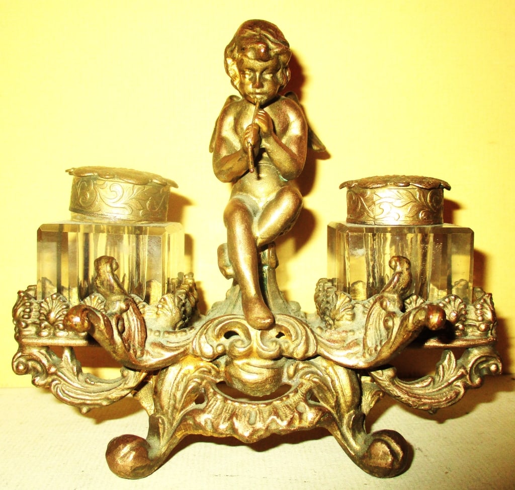 Victorian Ink Stand: Lot Consists of a Victorian Cast Metal Ink Stand With a Winged Boy, Unfortunately the Pen is Missing. Approximate Size is 4 1/2" Inches Tall and 5" Inches Wide. Fair to Good Condition.