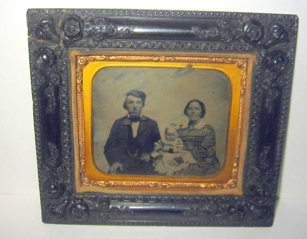 Victorian Amberotype in Gutta-Percha Frame: Victorian ambrotype or daguerreotype of Victorian family - mother, father and baby set in a gutta-percha frame. The frame has a crack in one corner, otherwise in good condition.