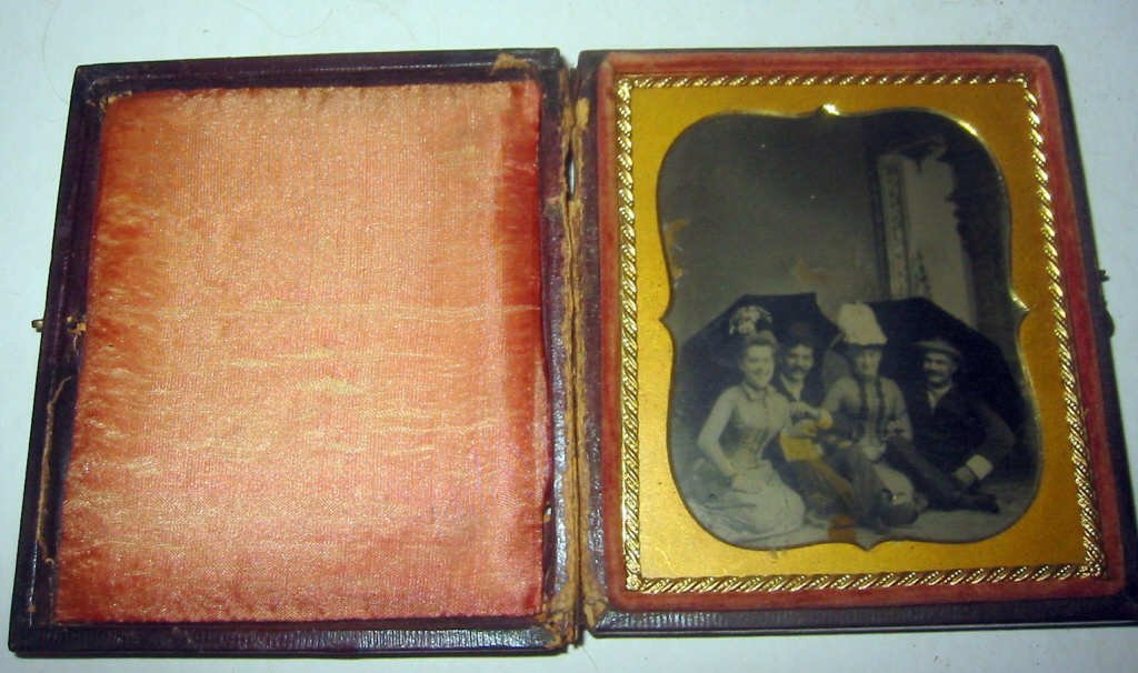 Daguerreotype/Ambrotype in Leather Case: Daguerreotype /Ambrotype of two young couples sitting under umbrellas in good condition - case has been separated at hinge seam.