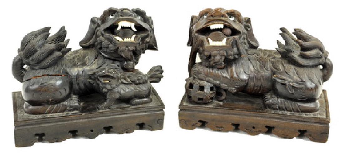Pair of Carved Wood Chinese Foo Dogs: 20th Century, bone teeth, glass eyes on carved wooden plinths, Crack on one dog, pieces of wood missing on other dog, 8 x 9 x 5.